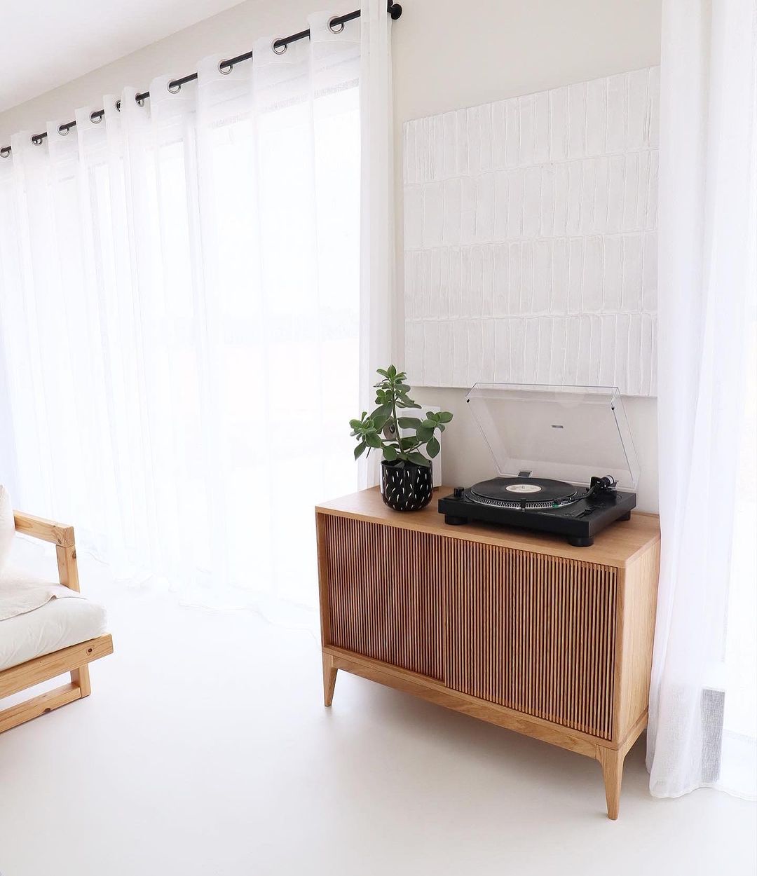 A wooden sideboard with a plant and a turntable in a bright, modern interior.pokoju.