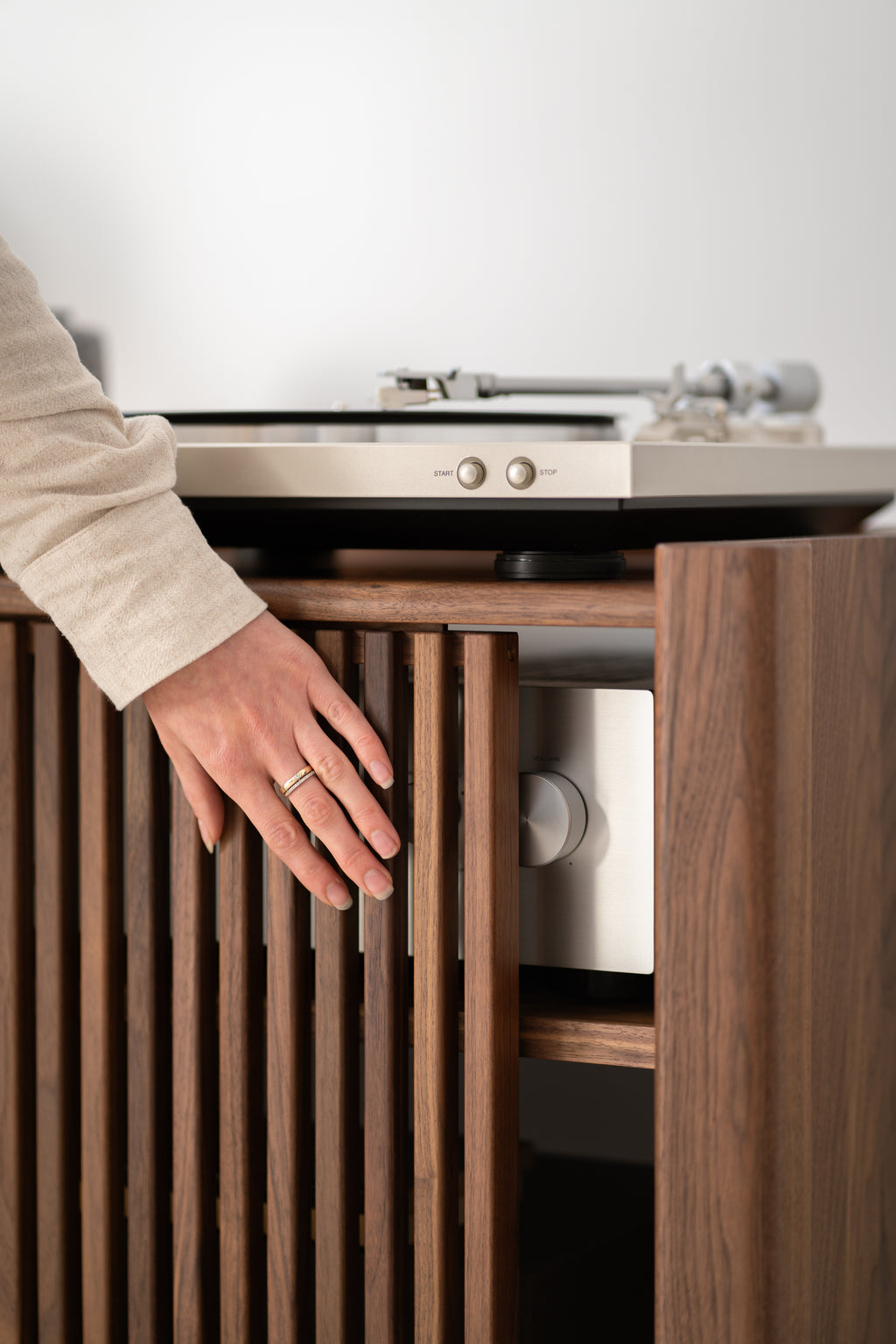 A hand touching wooden blinds next to a turntable.