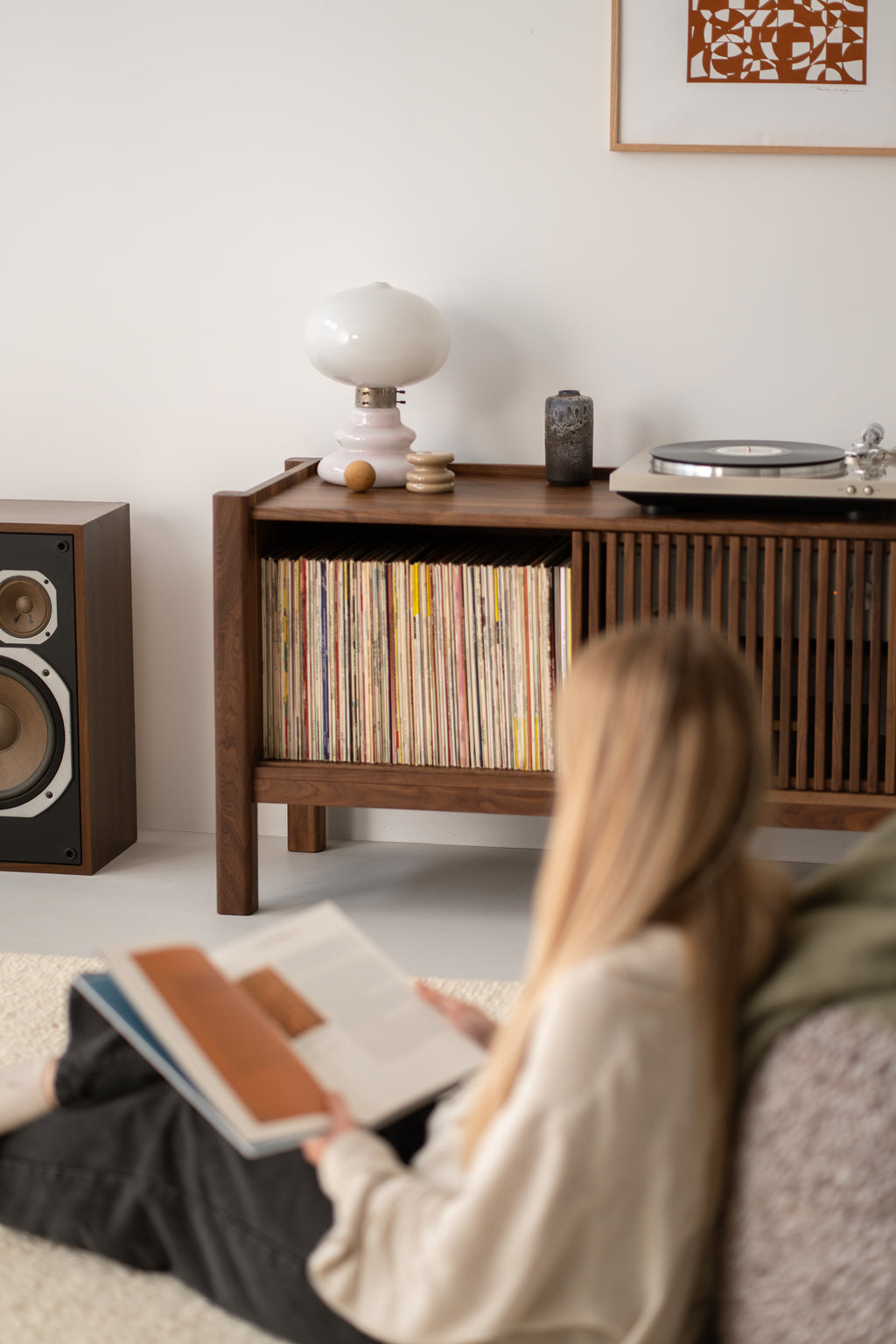 A person reading a book in a living room with a vinyl shelf and a turntable.