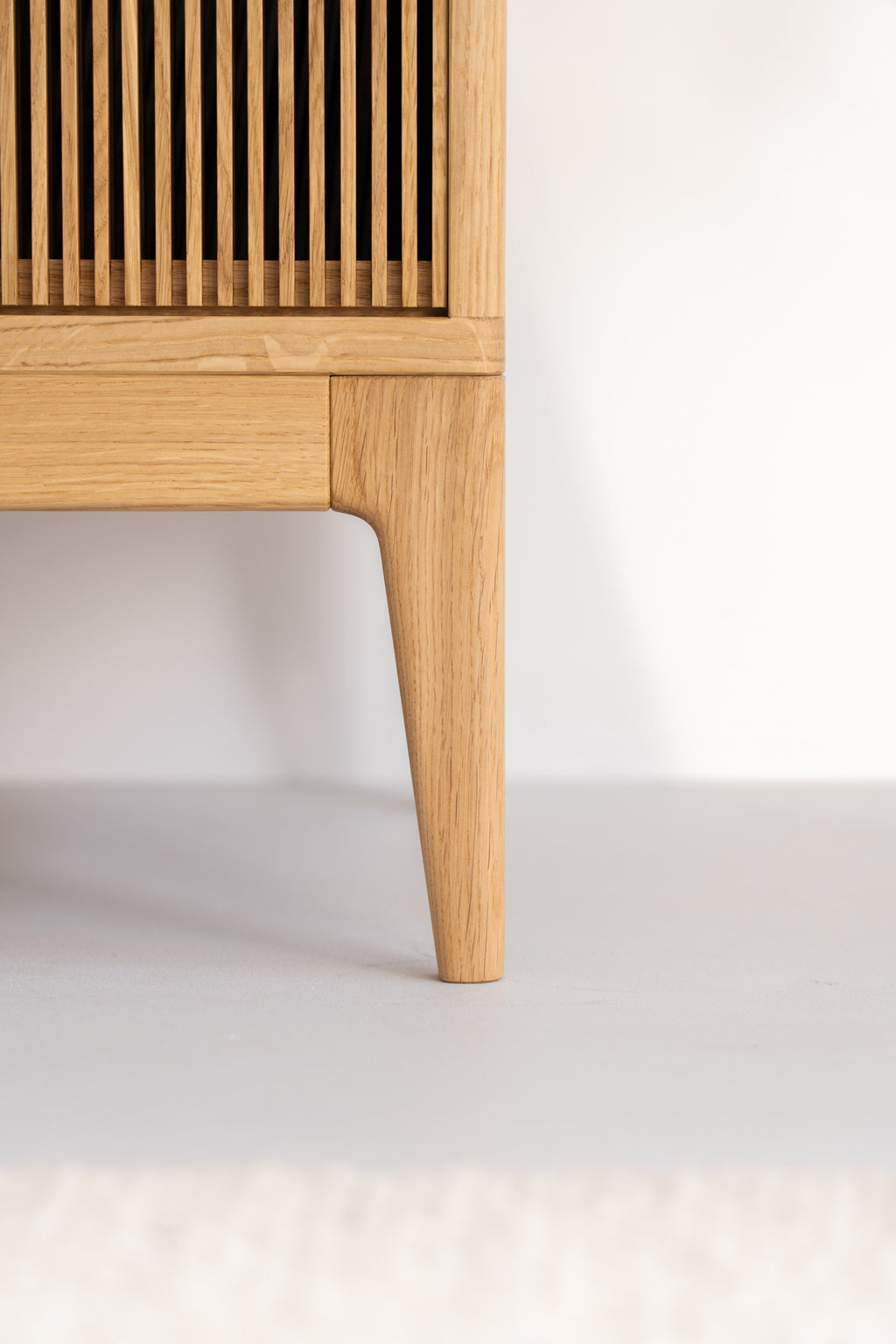 A wooden furniture leg with vertical slats in a light color.