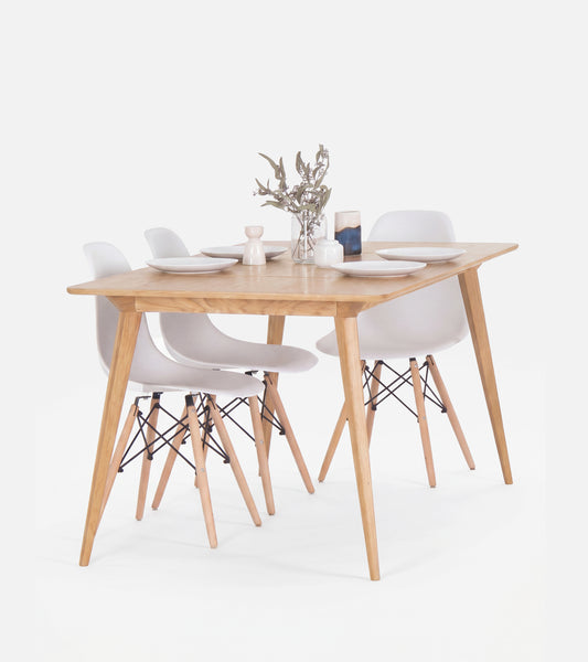 Wooden dining table set with four white chairs, set with plates and a small flower vase.