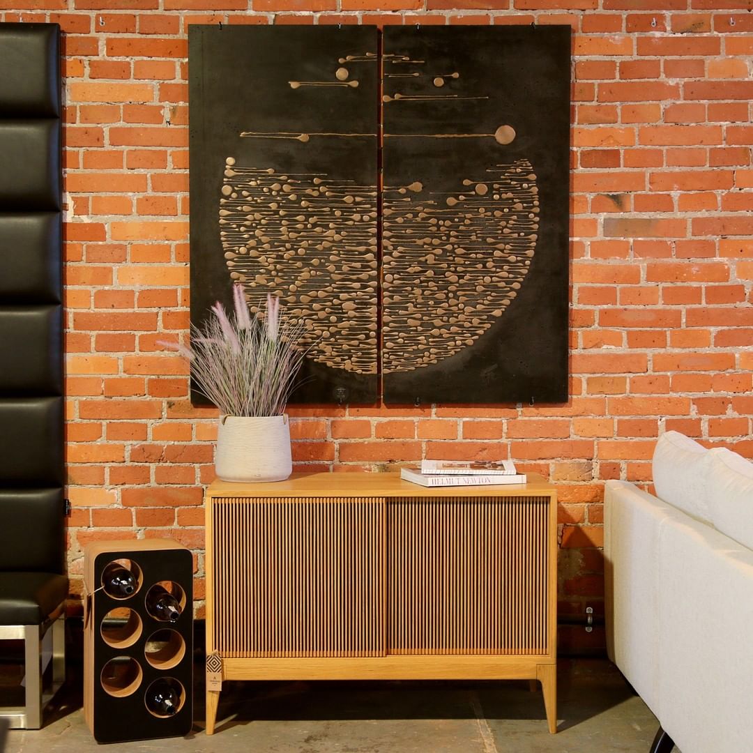 A cabinet with books and a potted plant against a brick wall with an abstract painting.