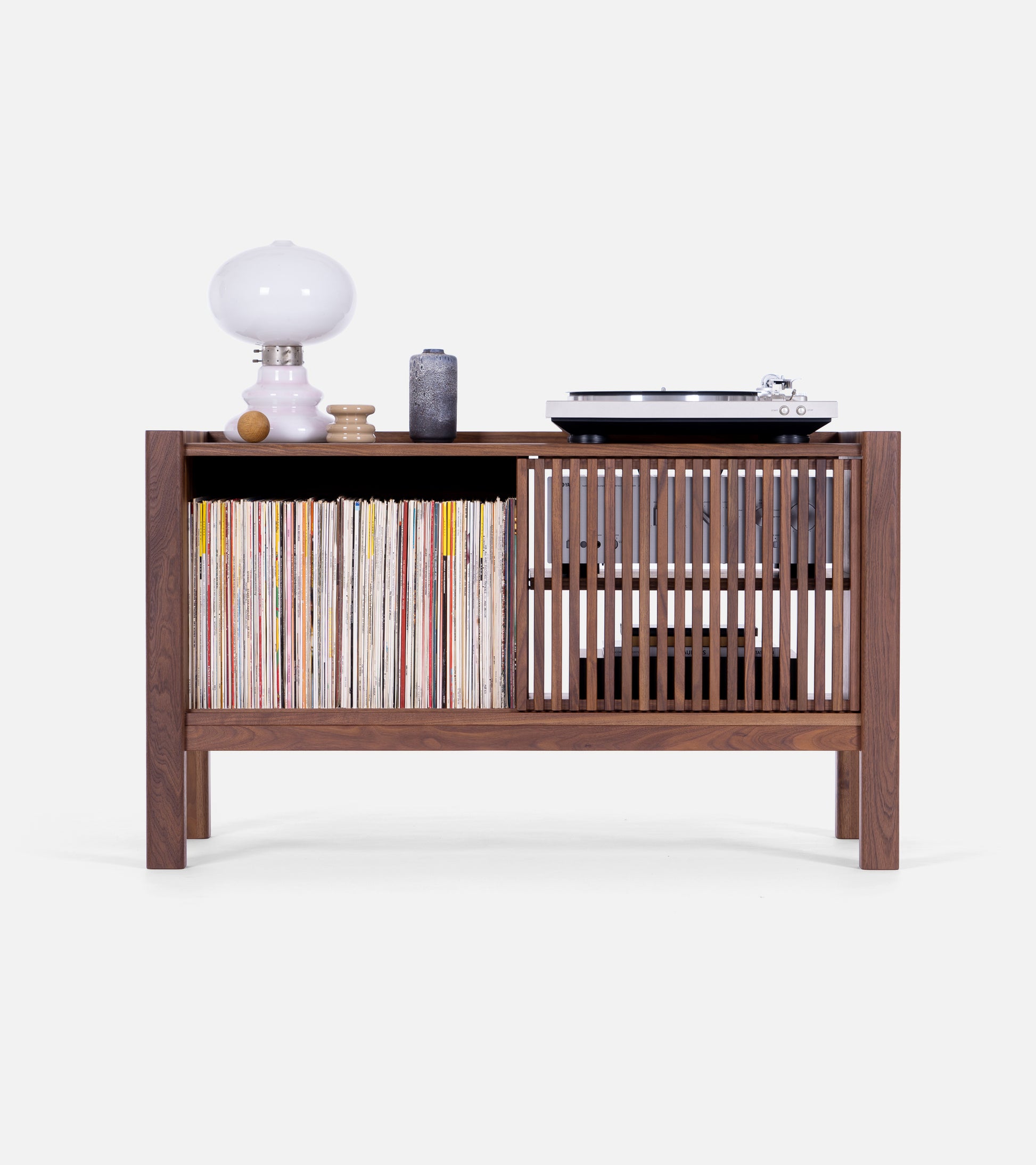 Wooden cabinet with vinyl records, slatted doors, a table lamp, and a turntable on top.