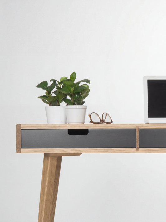 HEIM 140 desk in oak wood, close-up of a black drawer front and cut-out grip below plants and glasses