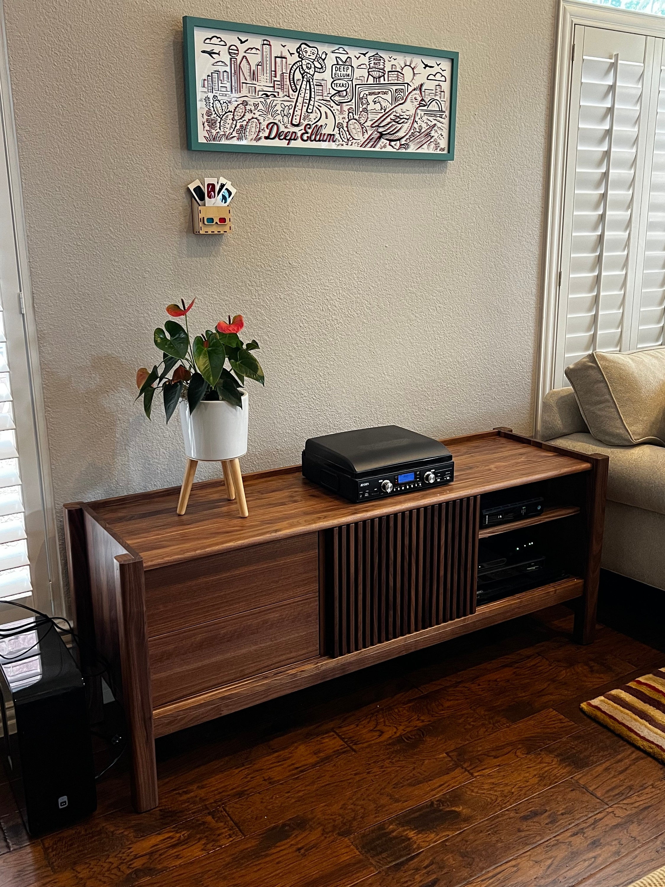 A sideboard with a potted plant, a turntable, and a wall artwork with the text "Deep Ellum".