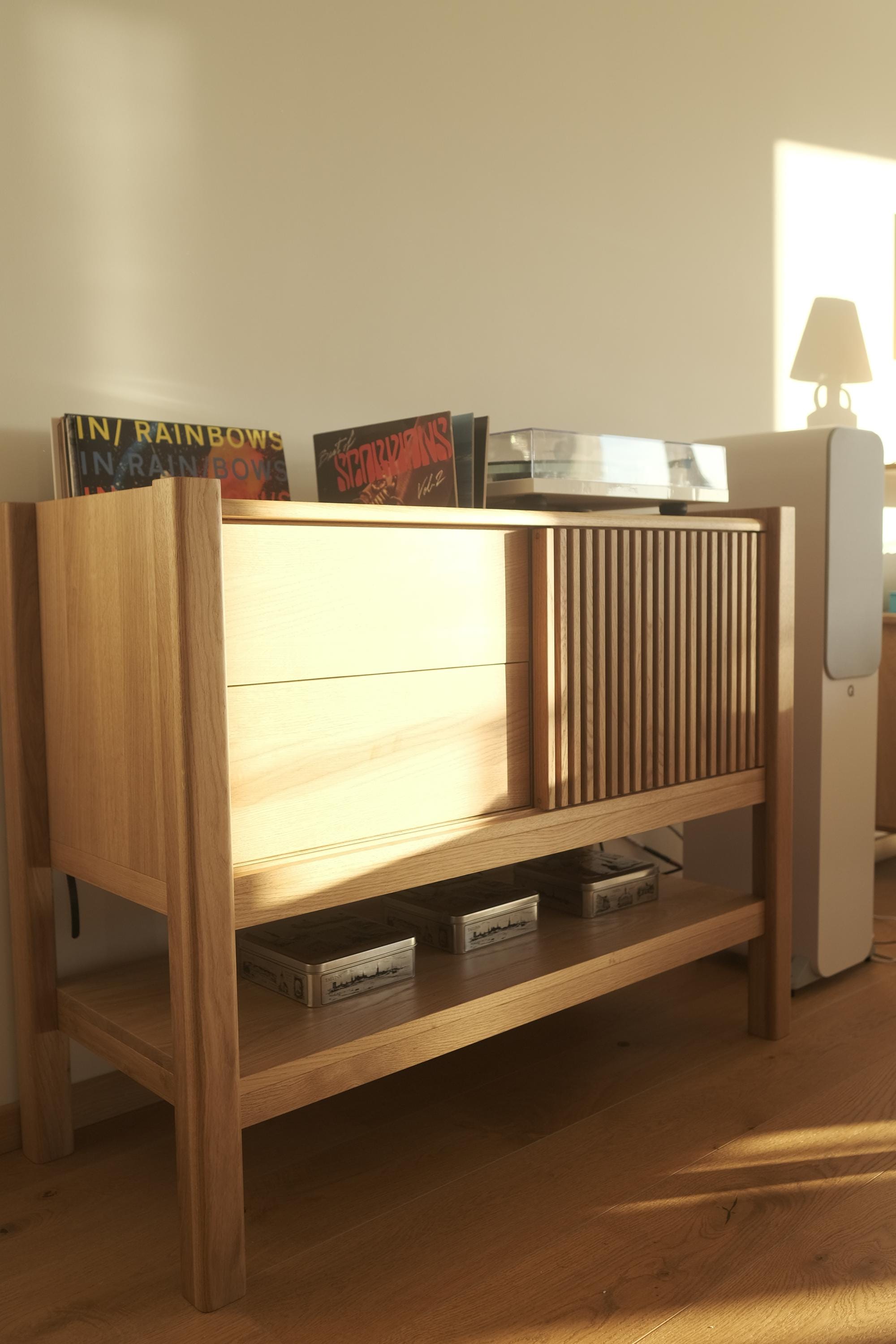 Wooden cabinet with vinyl records and a turntable, in warm lighting.