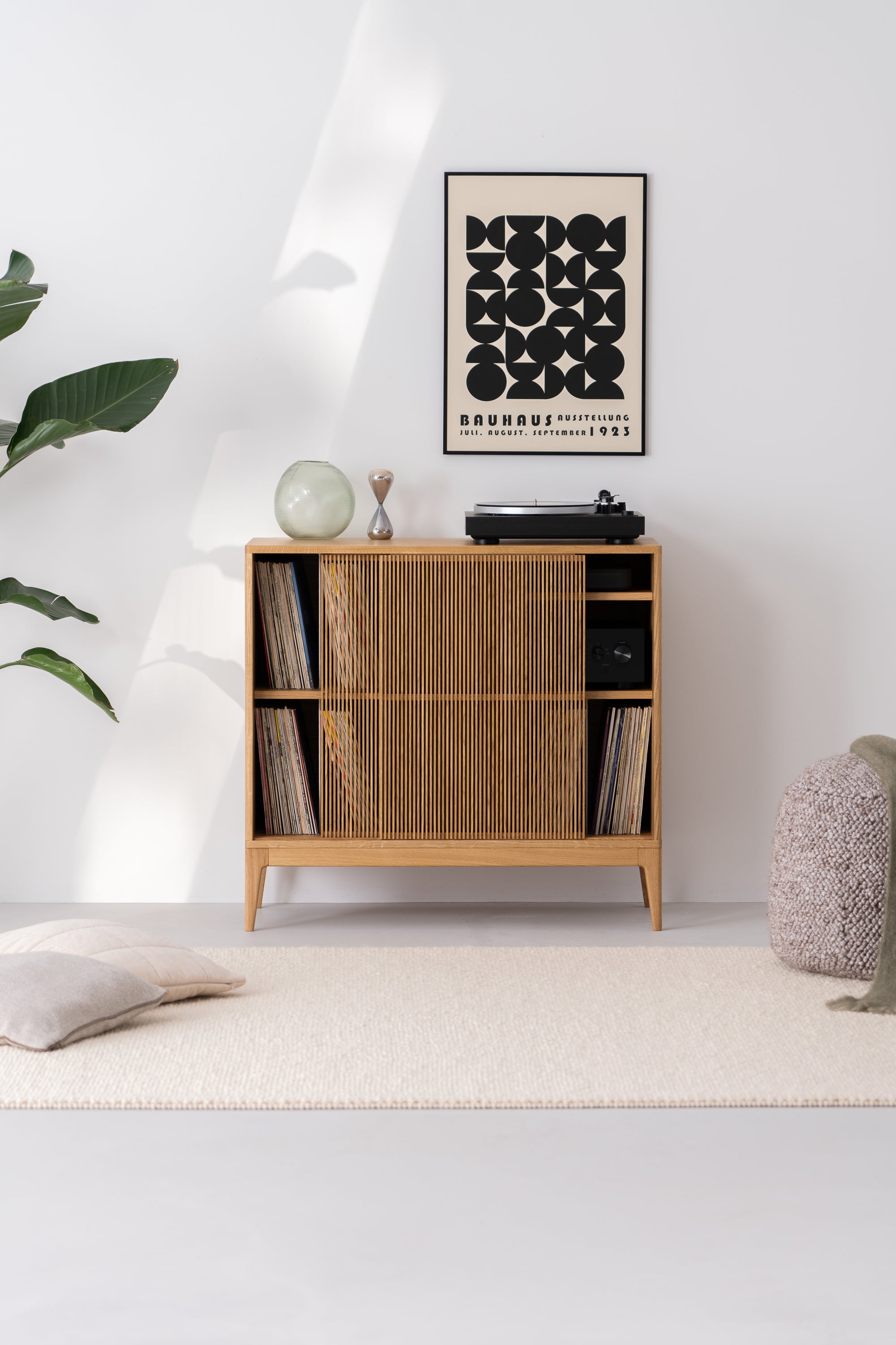 Minimalist living room with a wooden cabinet, vinyl records, Bauhaus poster, and plants.
