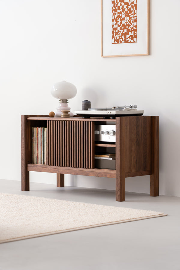 Mid-century modern console with records, a lamp, and a turntable. Framed abstract art hangs above.