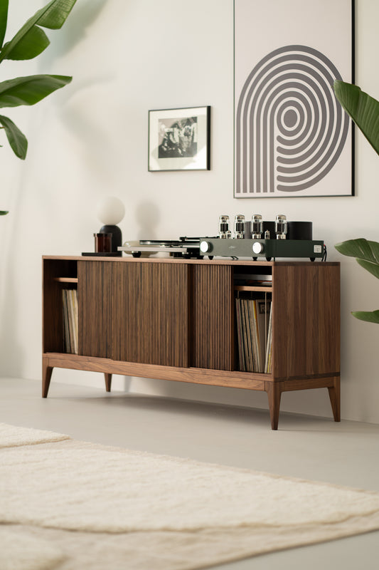 Mid-century modern cabinet with a record player and albums, set against a wall with framed art, and surrounded by green plants.