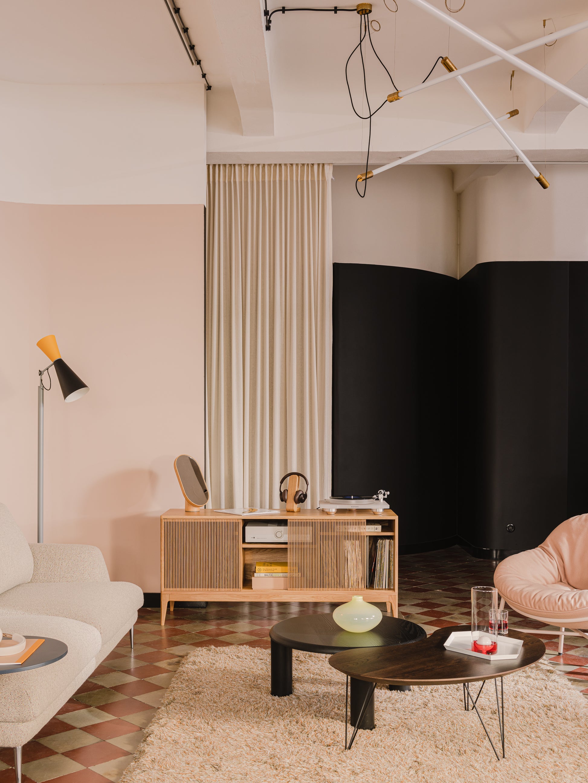 Modern living room with stylish furniture, beige sofa, wooden sideboard, black and wooden tables, and abstract lighting.