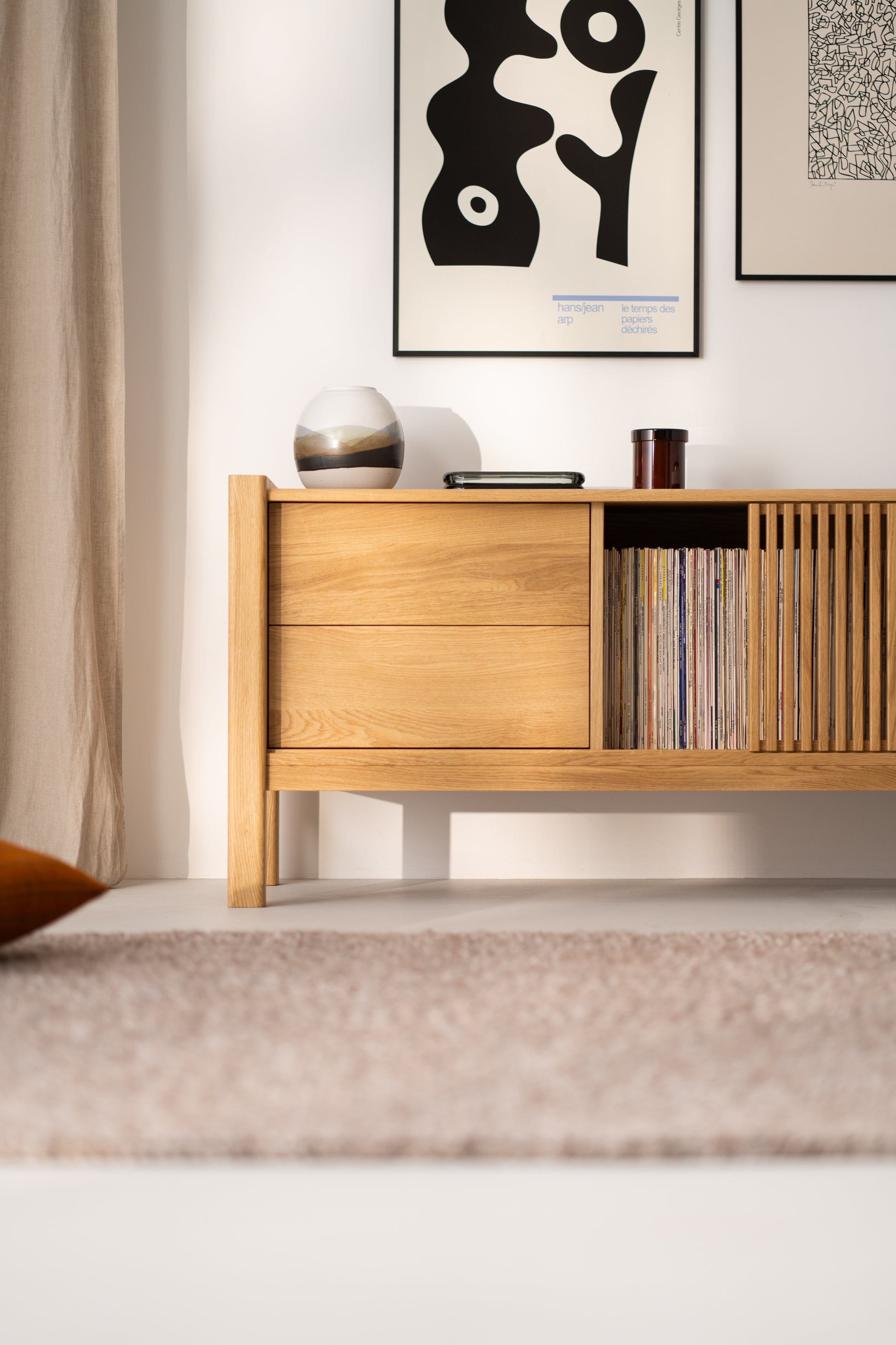 Minimalist wooden cabinet with decor, vinyl records, and framed artwork hanging on the wall.