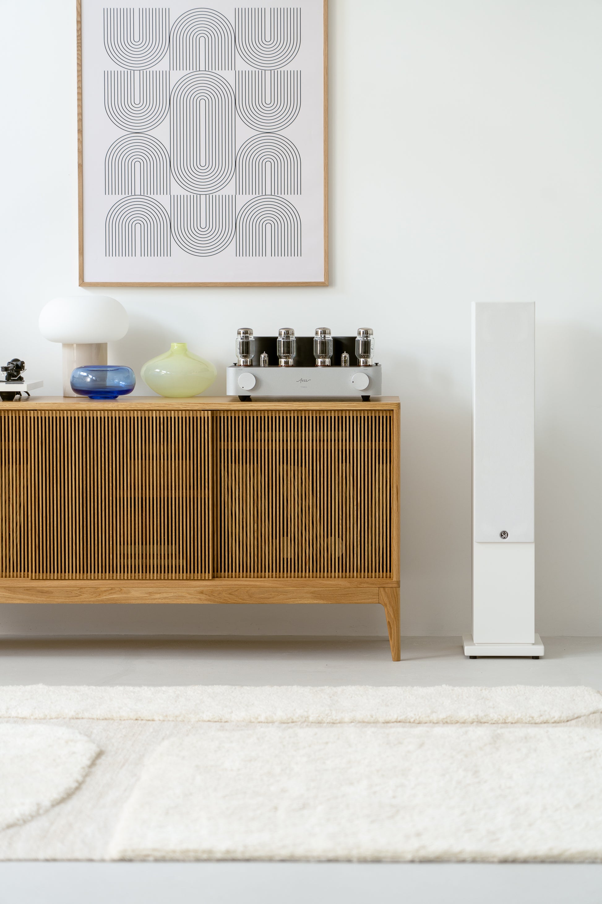 Modern living room with wooden cabinet, decorative vases, lamp, and framed abstract art on the wall.