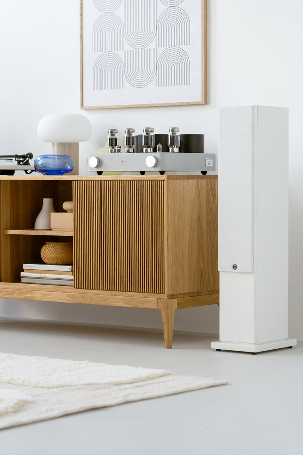 Mid-century modern room with wooden console, tube amplifier, abstract wall art, and a white speaker.