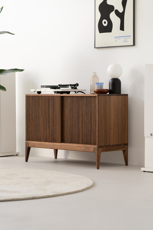 Mid-century modern cabinet with a turntable, lamp, and decor items on top, against a white wall with abstract art above.