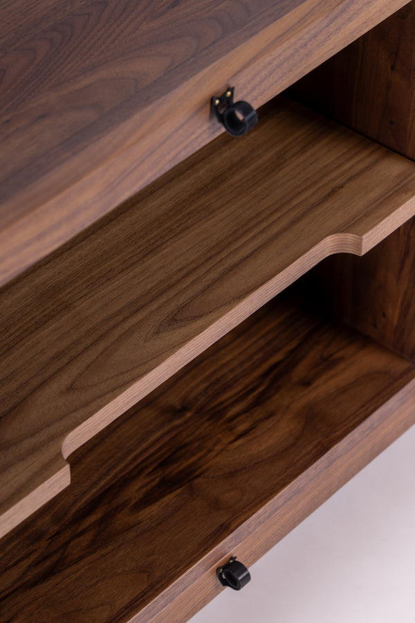 Close-up of a wooden cabinet with an open drawer, displaying smooth wood grain and black knobs.