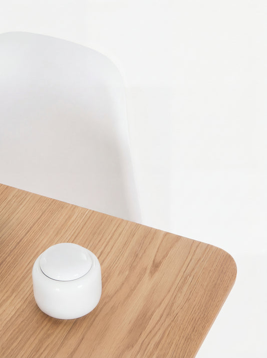 Minimalist wooden table with a small white container and a white chair in the background.