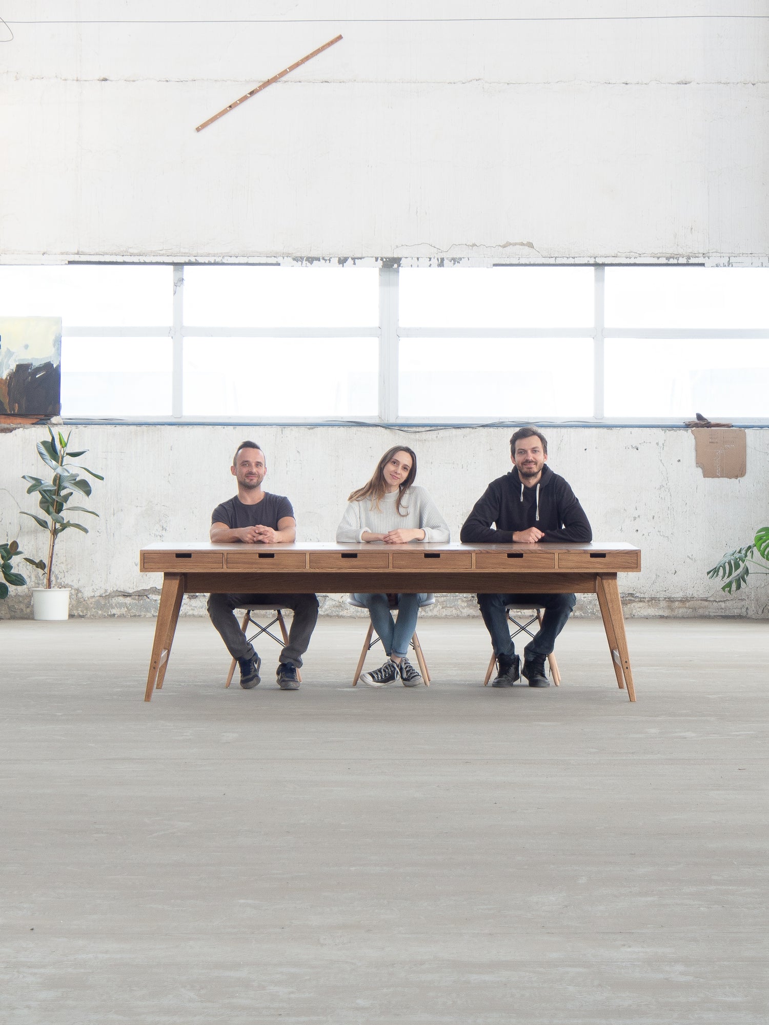 Three people sitting at a long wooden table in a bright, minimalist room.