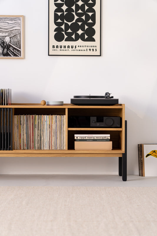 Wooden shelf with vinyl records, books, a turntable, and framed prints on a white wall.