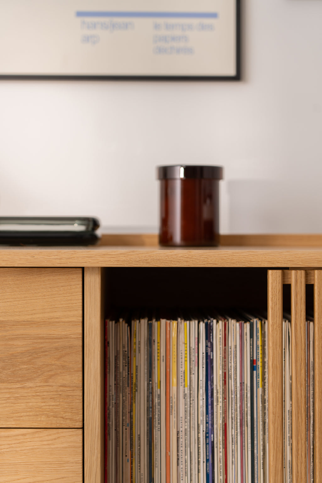 A shelf with vinyl records, with a brown jar and a laptop on top.