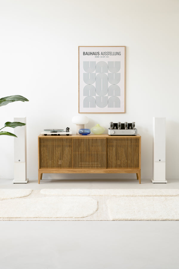 Minimalist living room with wooden sideboard, abstract framed art, speakers, plants, and modern decor items.
