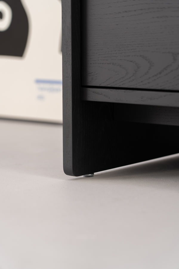 Close-up of the corner of a black wooden cabinet with adjustable metal feet on a grey floor.