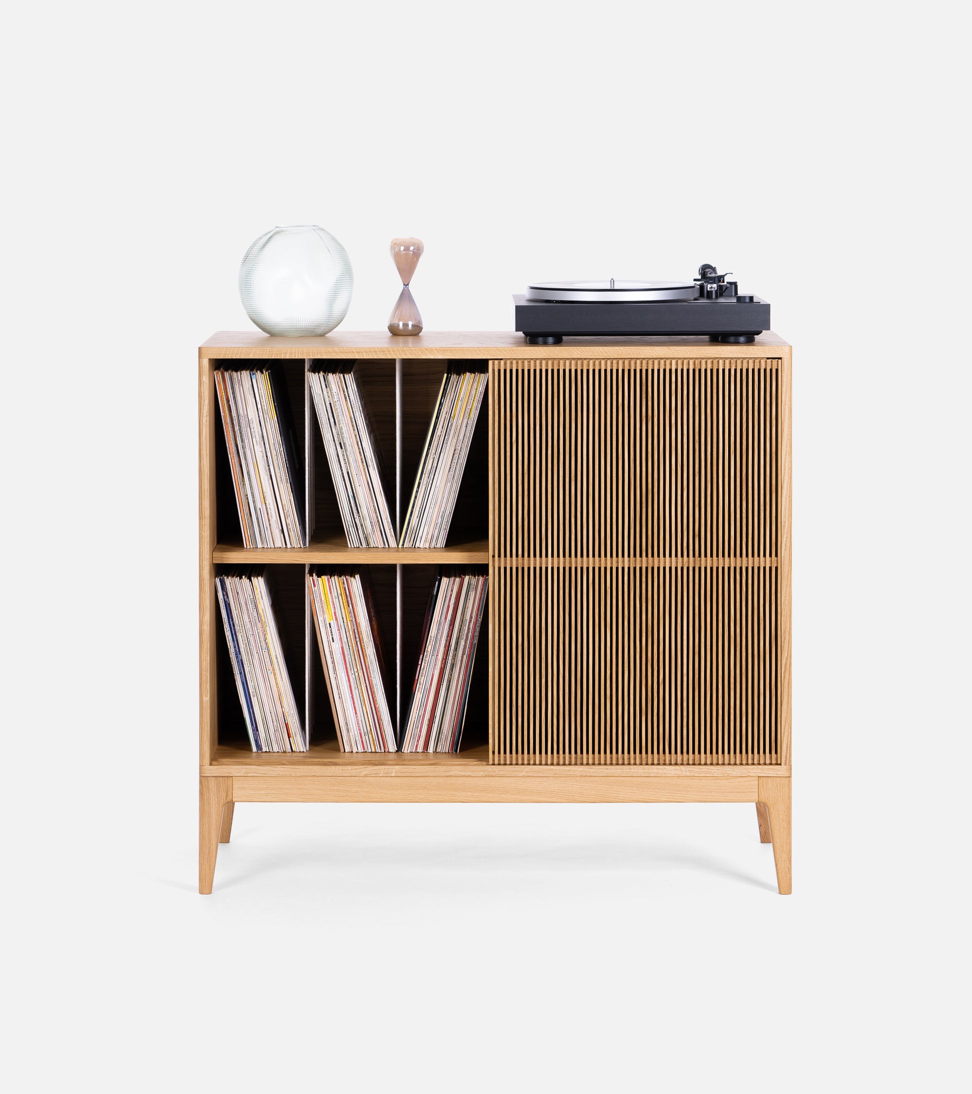 Wooden record cabinet with vinyl records, a turntable, a round vase, and an hourglass on top.