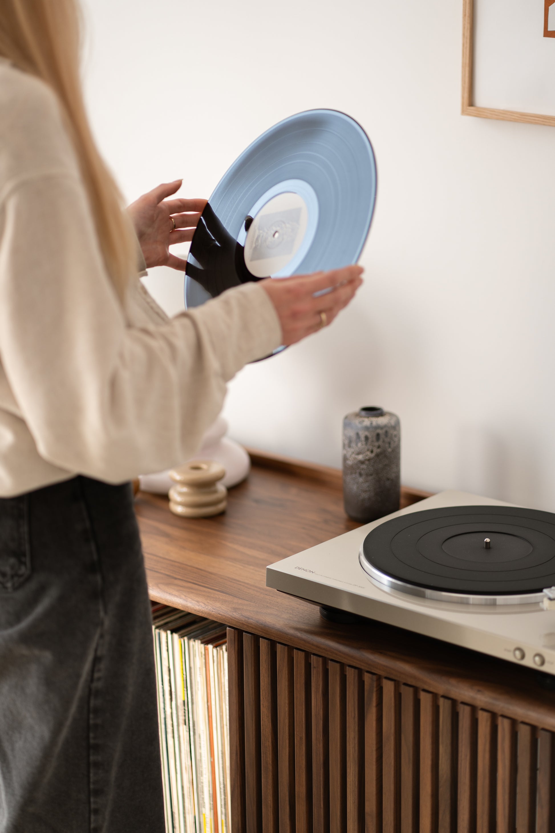 A person holding a vinyl record near a turntable on a wooden cabinet with stored records.