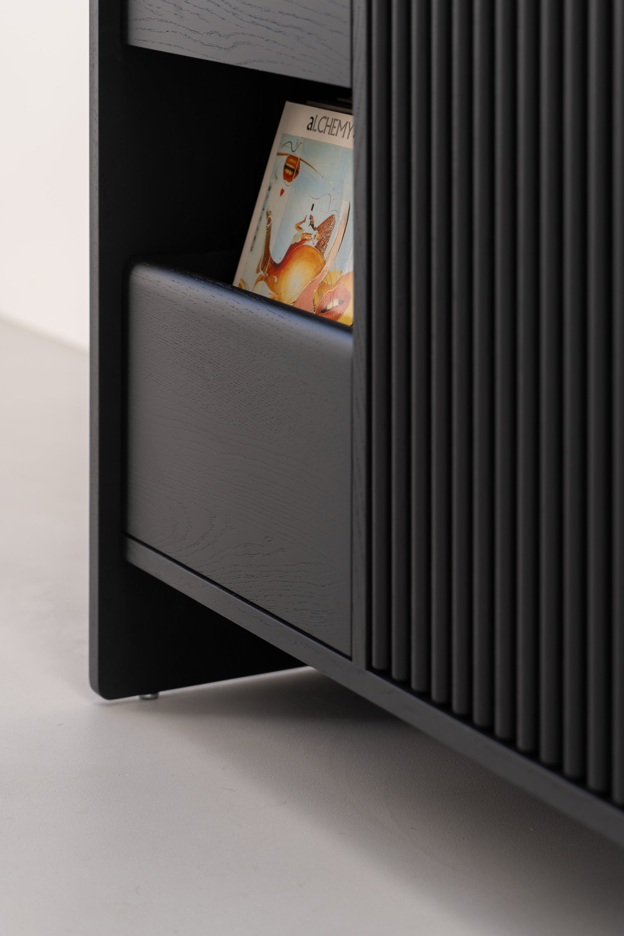 A close-up of a dark wooden shelf unit with a partially visible record titled "Alchemy" stored inside.