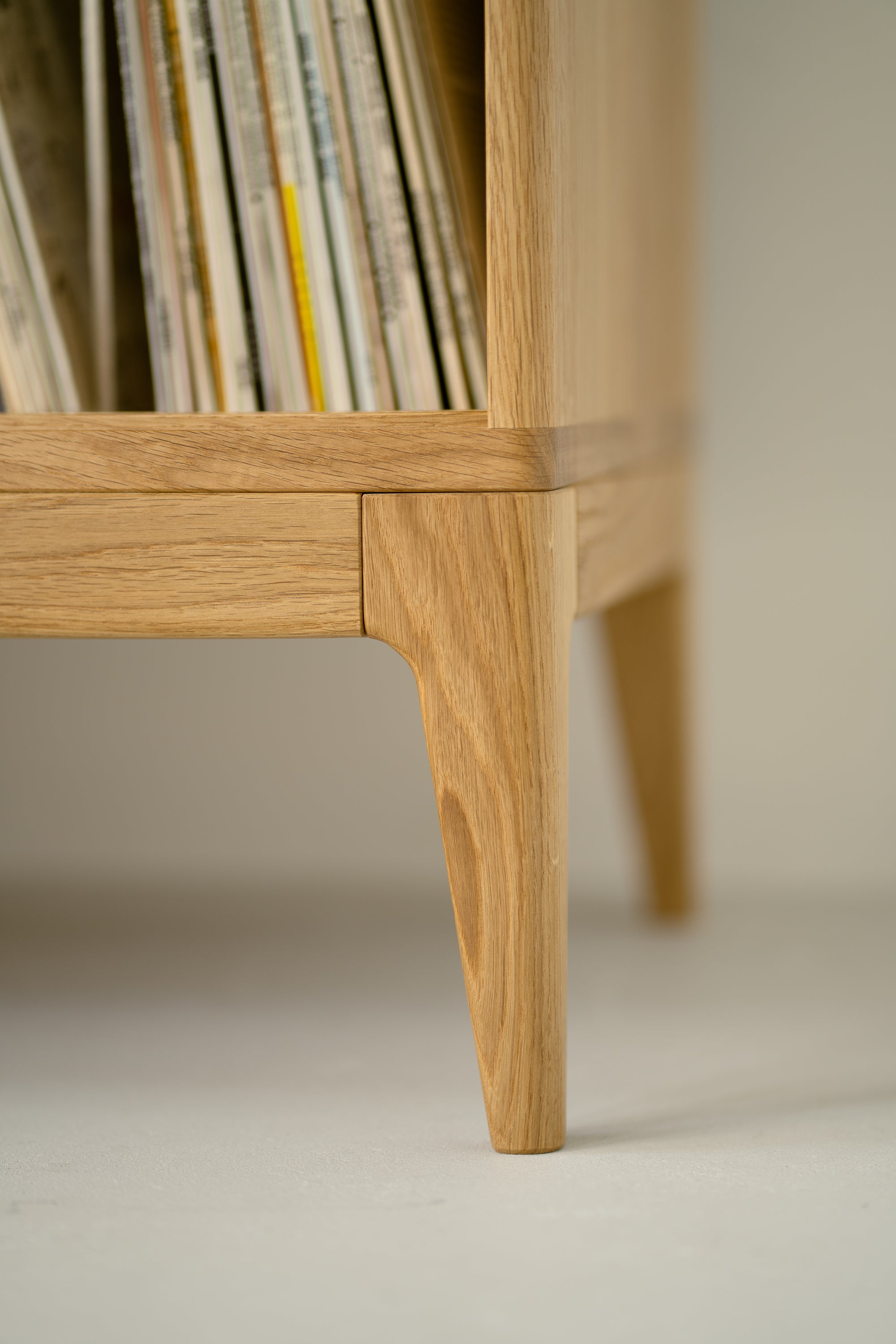 Close-up of a wooden cabinet leg and corner with books or records inside.