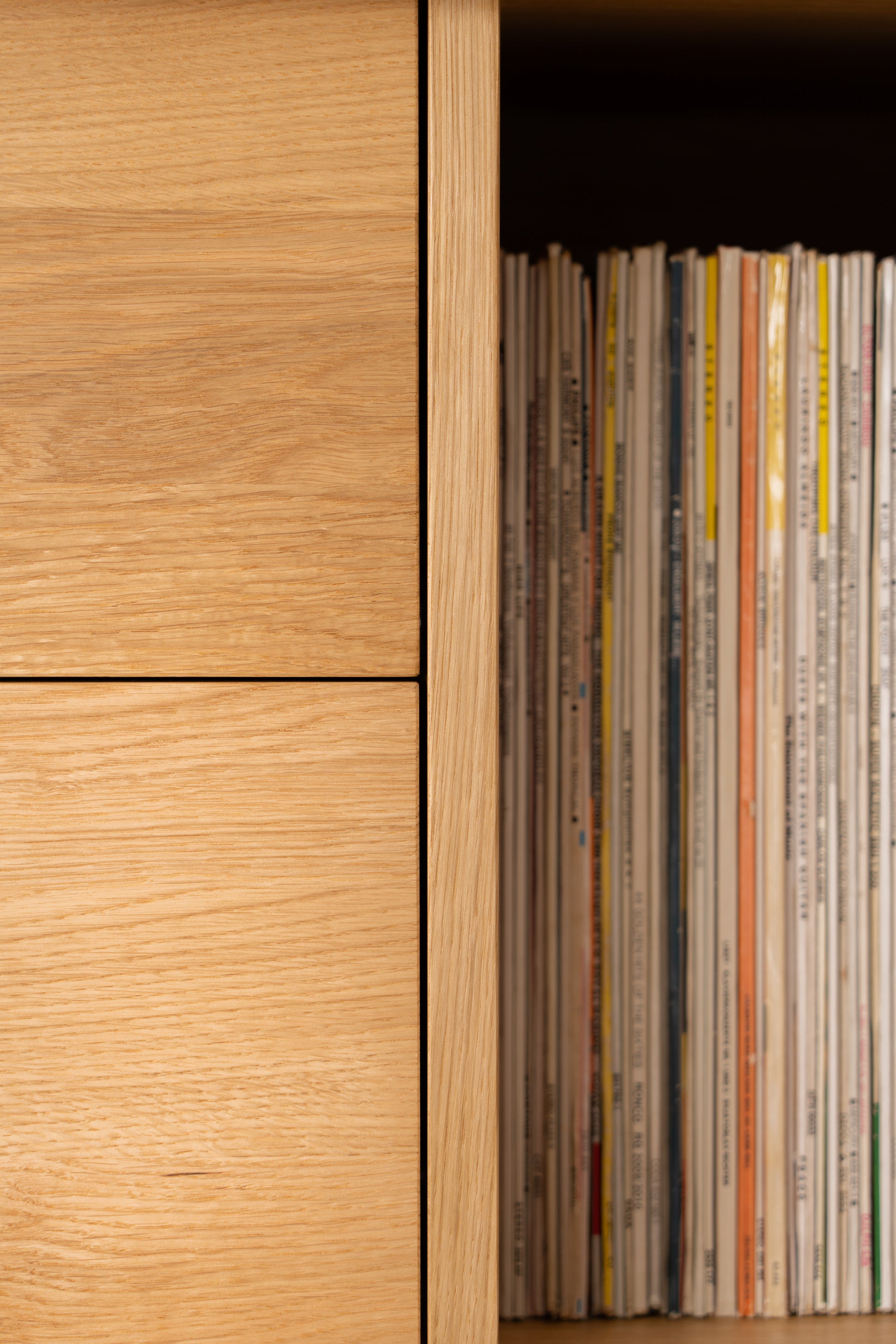 Close-up of a wooden bookshelf with a stack of vertically arranged vinyl records on the right side.