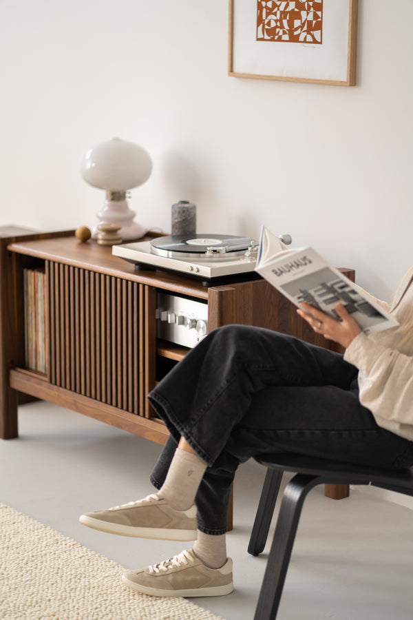Person reading a book near a wooden cabinet with a turntable and vinyl records, in a minimalist room.