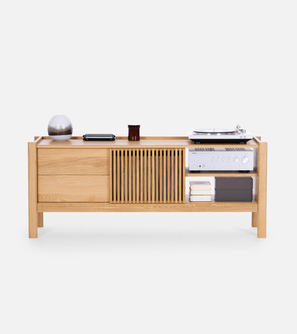 A modern wooden sideboard with drawers, a slatted door, and open shelves holding electronics, books, and decor items.