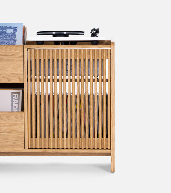 Wooden cabinet with vertical slats, holding vinyl records and a turntable on top.