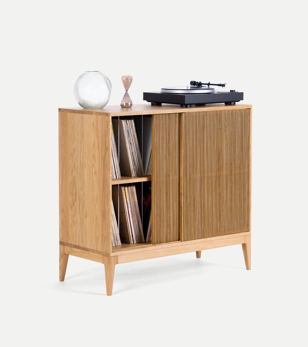 Wooden cabinet with records inside, a glass vase, hourglass, and record player on top.