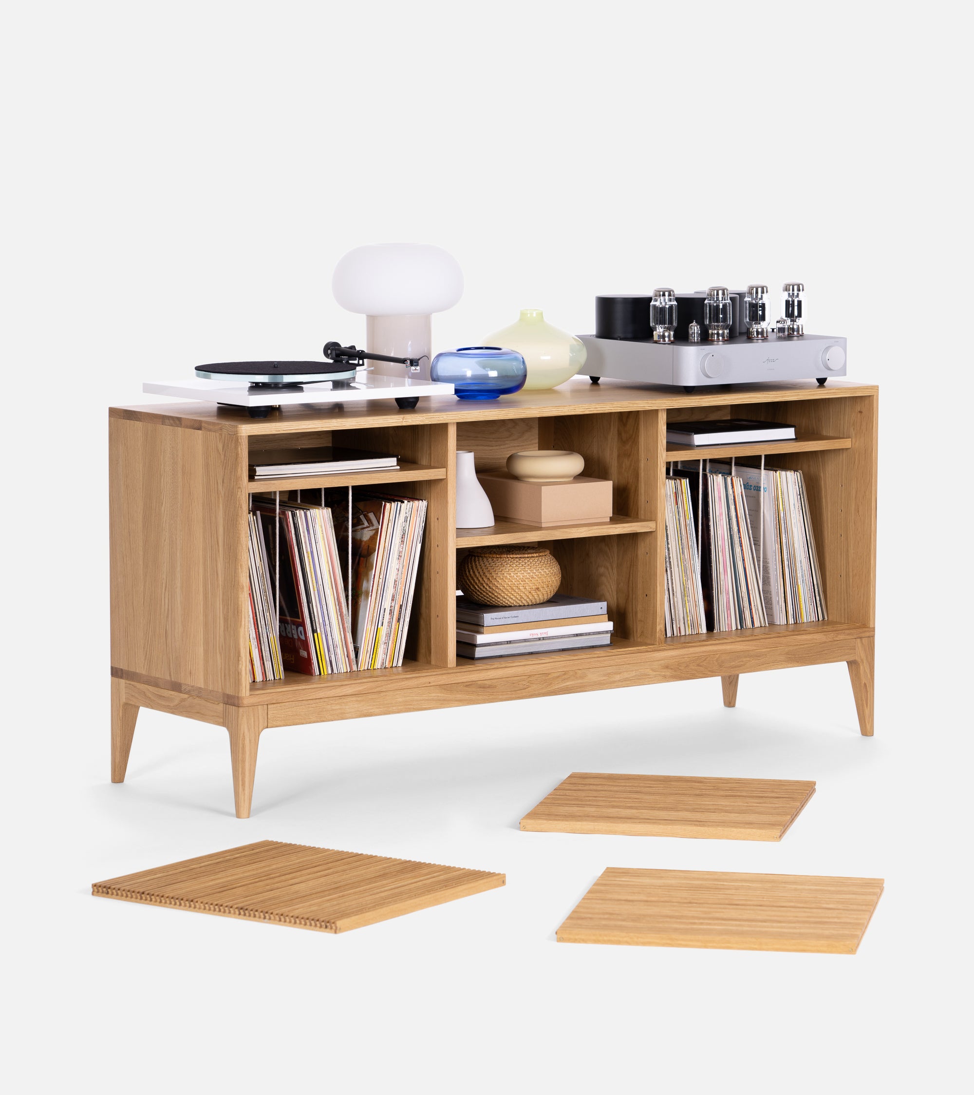 Wooden cabinet with records, books, and decorative items. A phonograph and lamp are on top, and wooden planks lay in front.