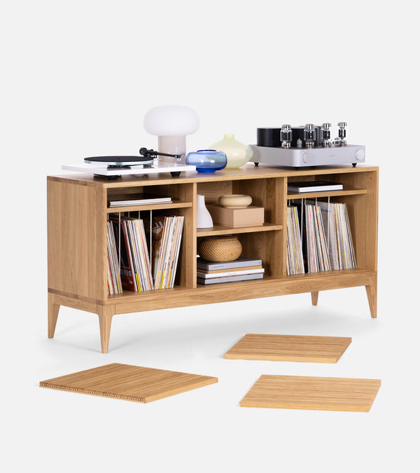 Wooden cabinet with records, books, and decorative items. A phonograph and lamp are on top, and wooden planks lay in front.