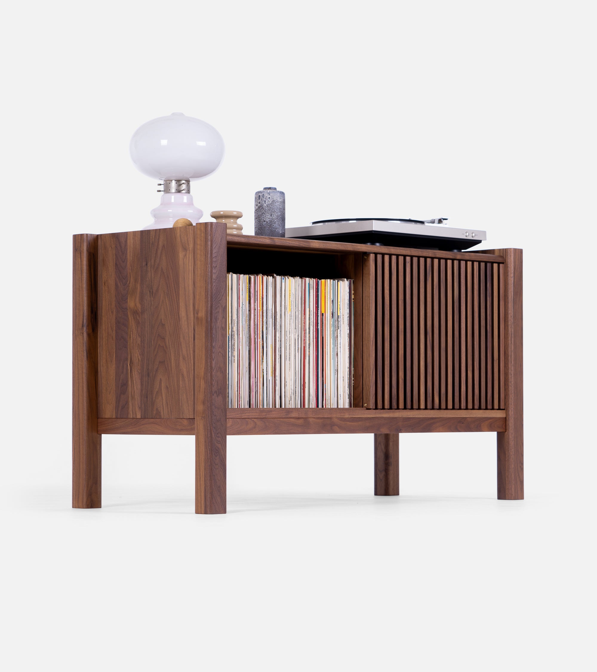 Wooden cabinet with vinyl records, a turntable, a white lamp, and small decorative items on top.