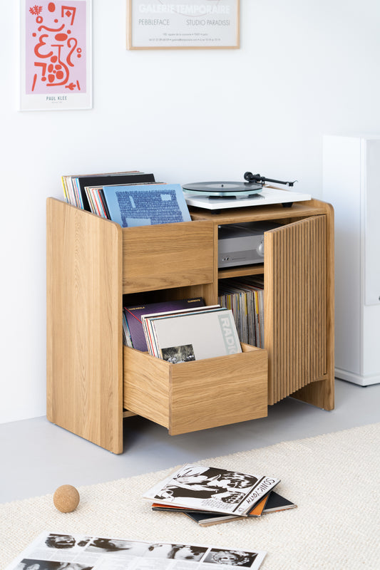 A wooden vinyl record storage unit with records and a turntable, standing on a light-colored rug with some records on the floor.