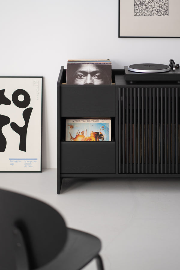 Black sideboard with vinyl records, including "Alchemy" by Dire Straits, a turntable on top, and framed art on the floor.
