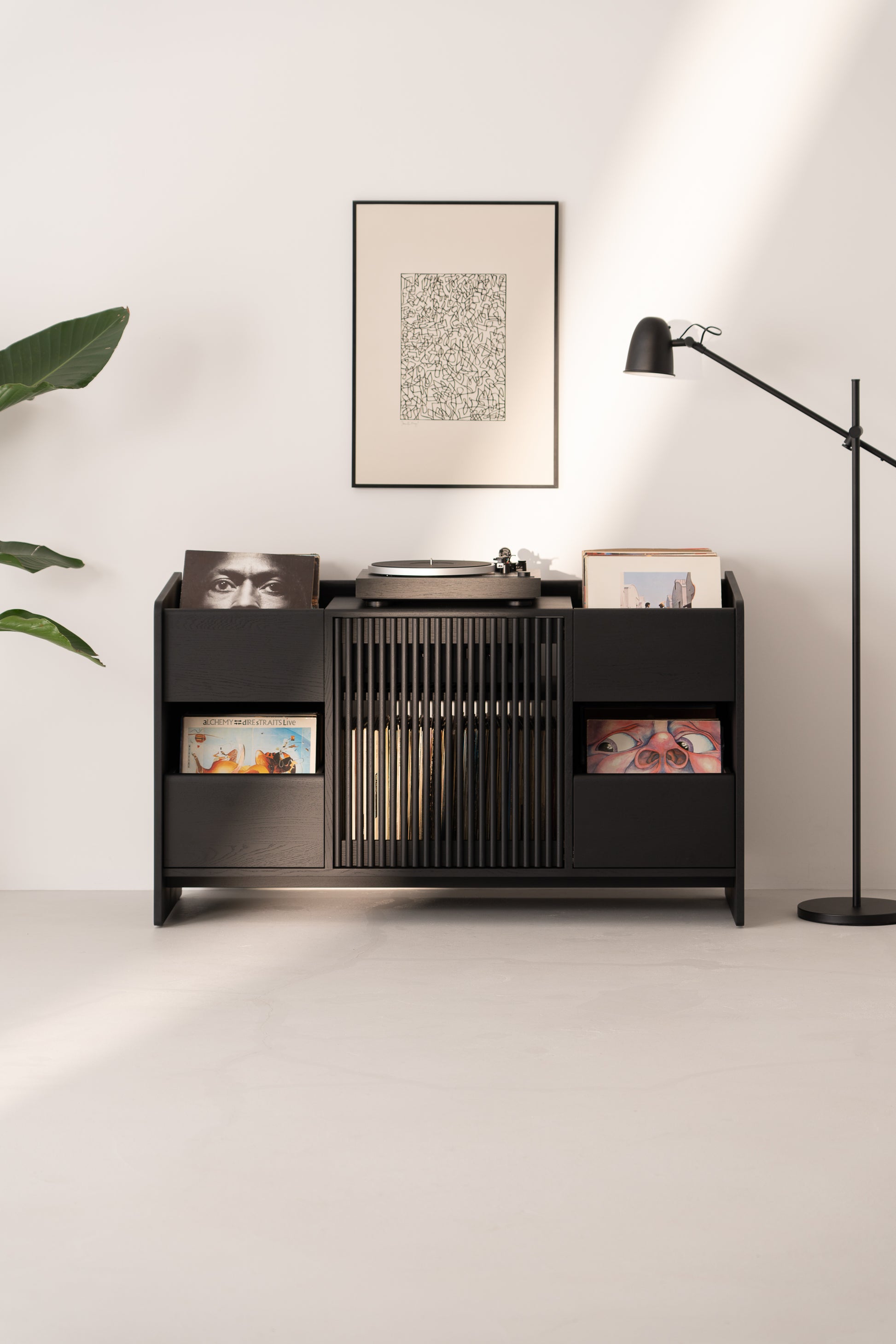 Minimalist vinyl record storage unit with turntable, framed art, floor lamp, and plant in a modern, well-lit room.