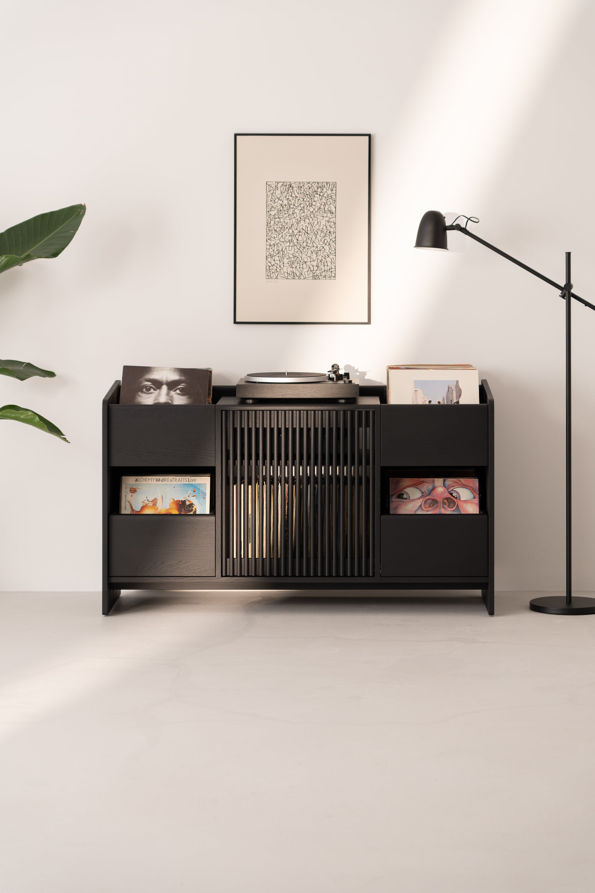 Minimalist vinyl record storage unit with turntable, framed art, floor lamp, and plant in a modern, well-lit room.