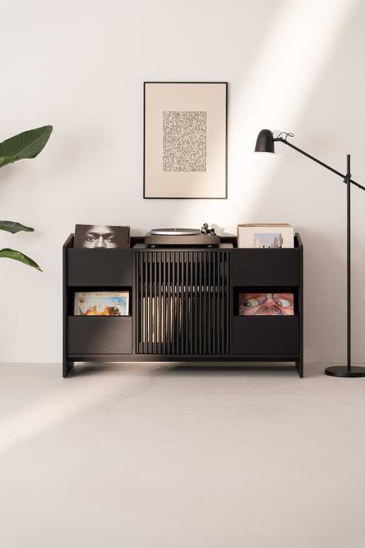 Minimalist vinyl record storage unit with turntable, framed art, floor lamp, and plant in a modern, well-lit room.