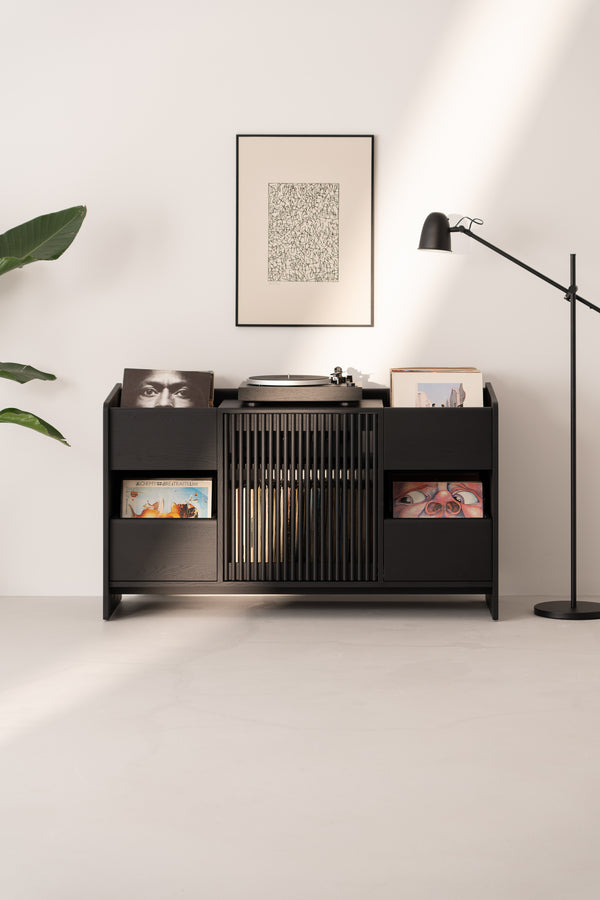 Minimalist vinyl record storage unit with turntable, framed art, floor lamp, and plant in a modern, well-lit room.