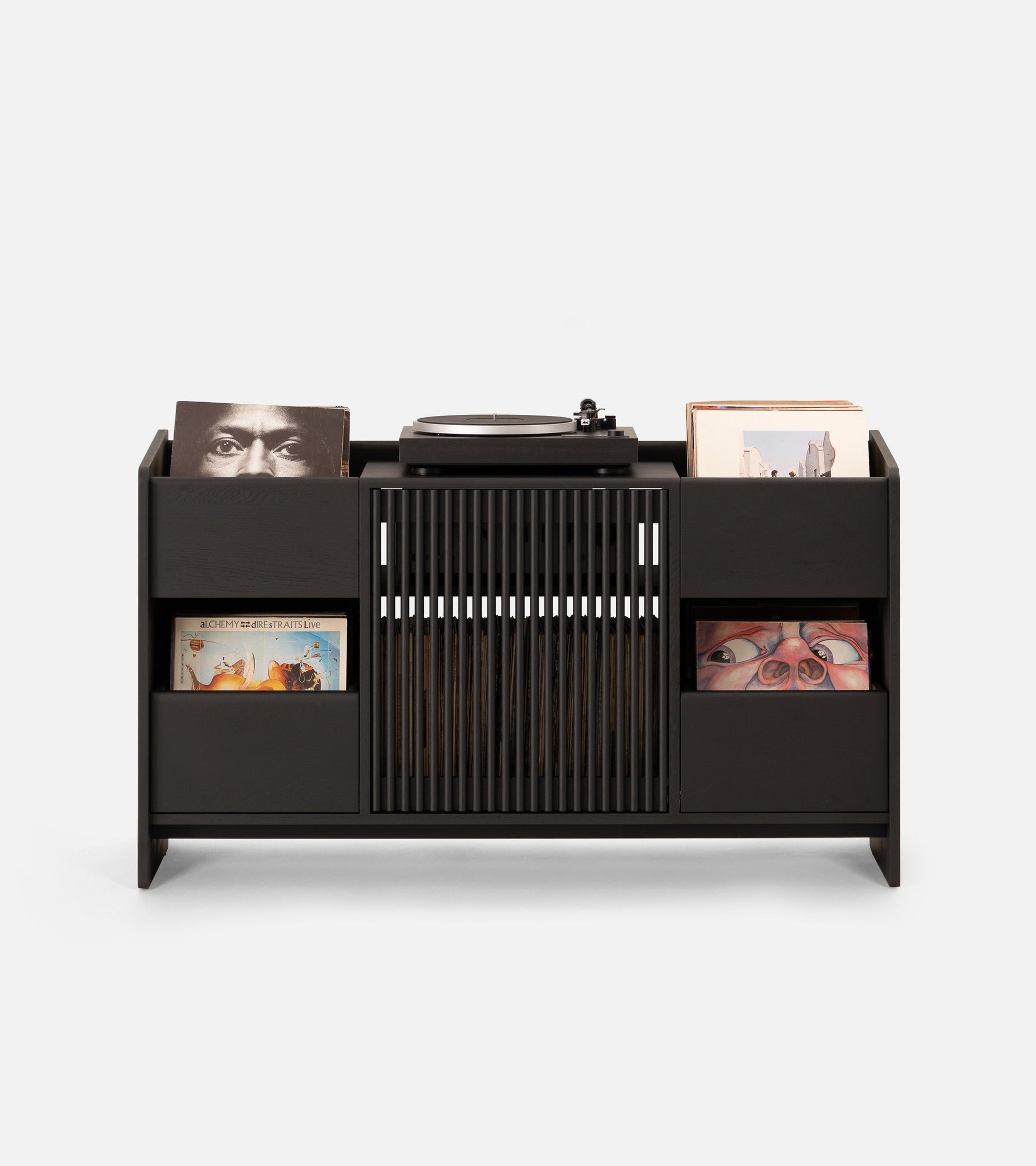 A modern vinyl record player setup with a black storage unit, a floor lamp, and framed artwork on a minimalist wall.