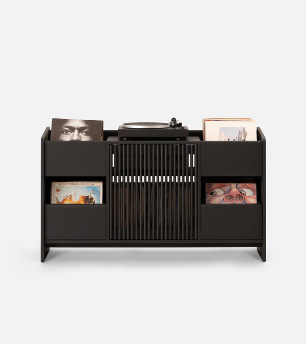 A modern vinyl record player setup with a black storage unit, a floor lamp, and framed artwork on a minimalist wall.