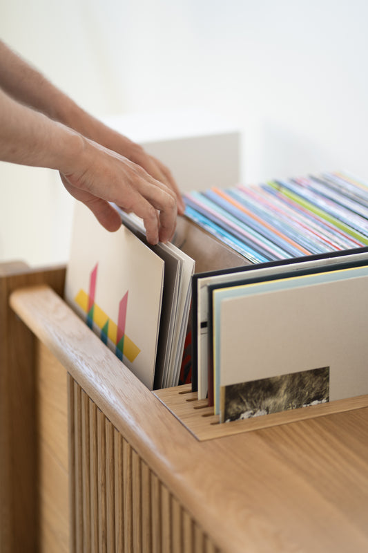 Hands flipping through vinyl records in a wooden storage box.