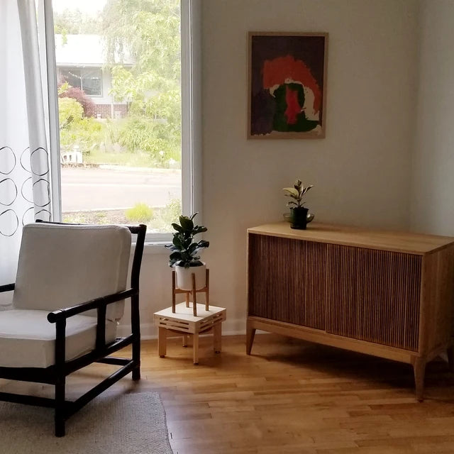 A modern interior with a white armchair, plants, a wooden cabinet, and a painting on the wall.