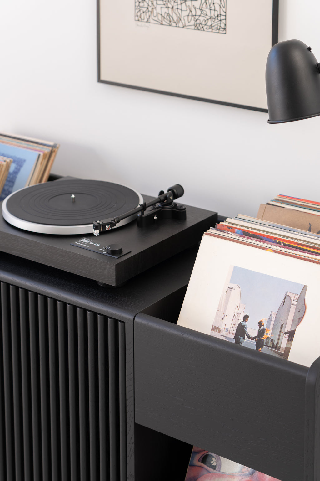 A turntable on a sideboard next to a collection of vinyl records and a painting on the wall.