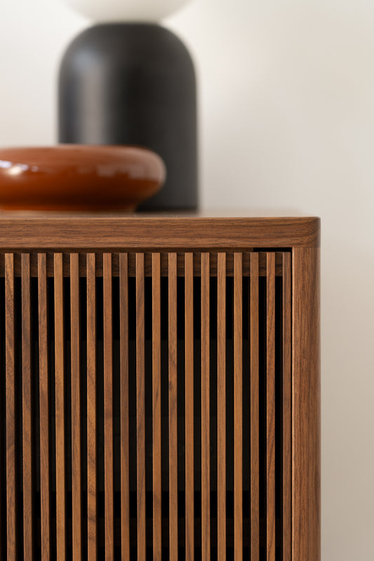 Close-up of a wooden cabinet with a slatted front design, topped with a brown and black decorative item.