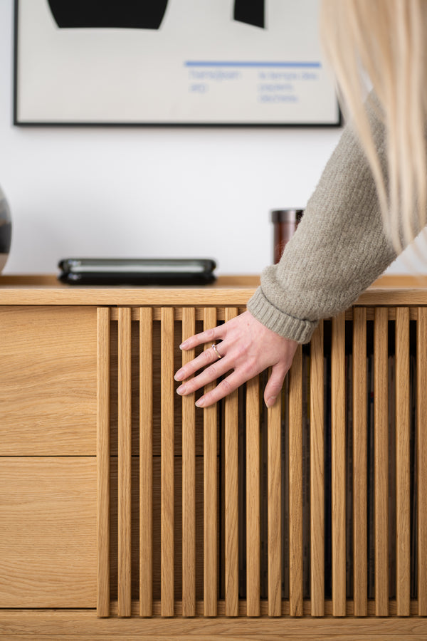 Hand touching a wooden cabinet with vertical slats, framed artwork on the wall above.